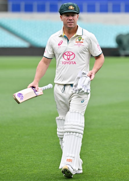 David Warner, in full Test whites and pads, carries a bat and gloves as he makes his way to a team photo