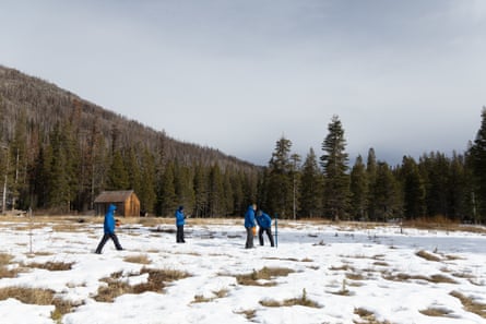 Four people in matching blue coats walk across a snowy field with grassy patches showing through.