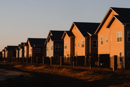 A row of new, two-story homes with peaked roofs seen in the rays of the setting sun.