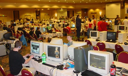 A room in a convention centre of hotel with rows of tables with large computers on and young people sitting at them