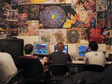 Three boys at computers with their backs to the camera, in front of a wall covered in posters
