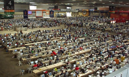 A hall in a convention centre with rows and rows of desks with computers on and people sitting at some of them