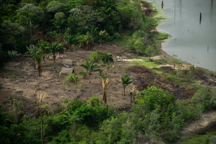 An aerial shot of a forest clearing by a river with two small huts visible