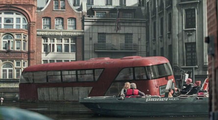 A still from The End We Start from, featuring a submerged London bus, with a dinghy full of people passing it, level with the top deck. 