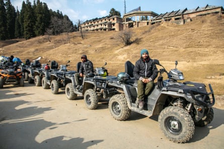 A young man sits idly on a four-wheeled all-terrain vehicle with a line of similar quad bikes and other drivers behind him 