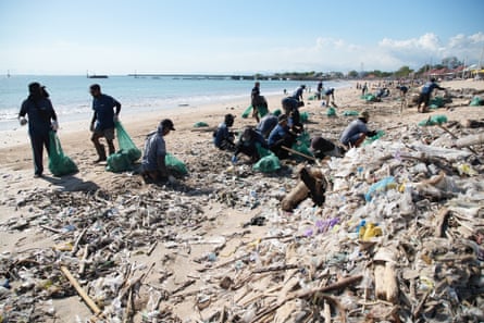 Piles of plastic on beach and people with green bin bags
