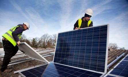 Workers position solar oanels on the roof of a house in preparation for installation