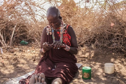 A Maasai woman sits on the ground in the shade doing beadwork