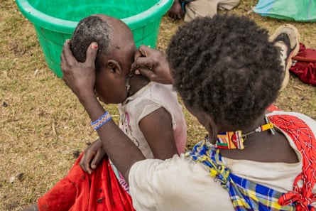 An older woman shave the head of a young child outside