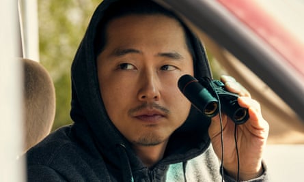 Asian man wearing black hoodie and holding binoculars.