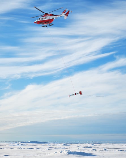 A torpedo shaped scientific instrument is carried by a helicopter.