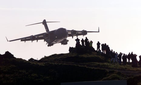 The silhouette of a huge transport plane approaching spectators watching from a low hill 
