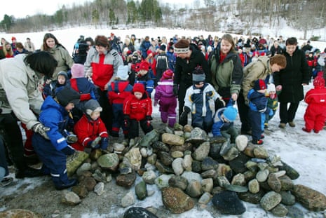 A big crowd of small children and adults putting stones on a grave in a snowy landscape