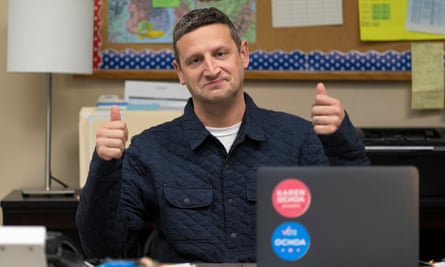 Tim Robinson seated at a desk raising both hands in thumbs-up gestures.