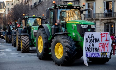 A row of tractors along a street with a protest banner in Spanish on the lead vehicle