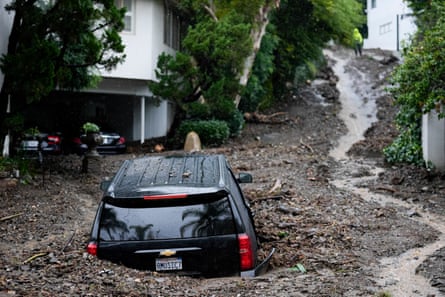 A hilly street with a black Ford SUV doors deep in mud.