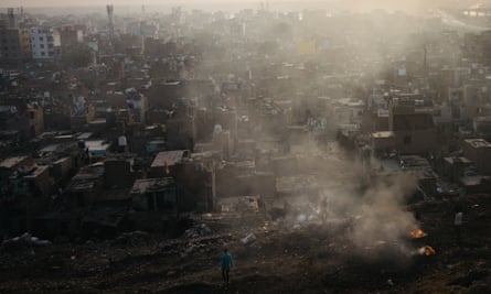 Smoke rises off the piles of rubbish, where there are small fires, from the Bhalswa landfill site against the backdrop of the city in the morning light, Delhi, 9 October 2023