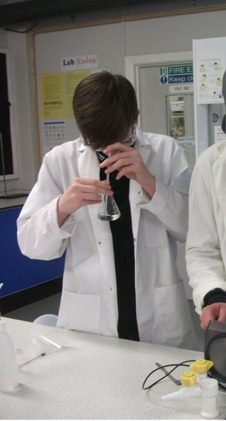 A teenage boy in a labcoat uses a pipette and a conical flask during a science experiment