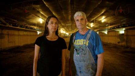 A man and a woman pose in a large warehouse