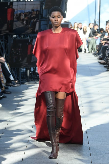 A model in a red gown, which is short at the front and long at the back, paired with brown thigh-high boots