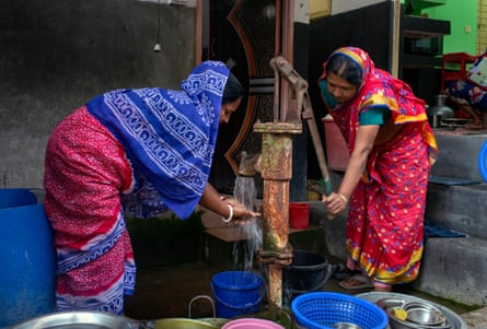 Two women in brightly coloured saris collect water from a pump