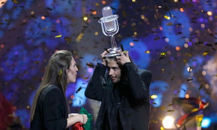 A man holds a large trophy on his head as a person next to him exclaims