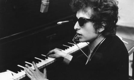 Bob Dylan sitting at a piano, wearing sunglasses