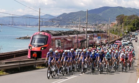 The peloton is passed by a pink Giro-branded train on the coastal road to Lucca.