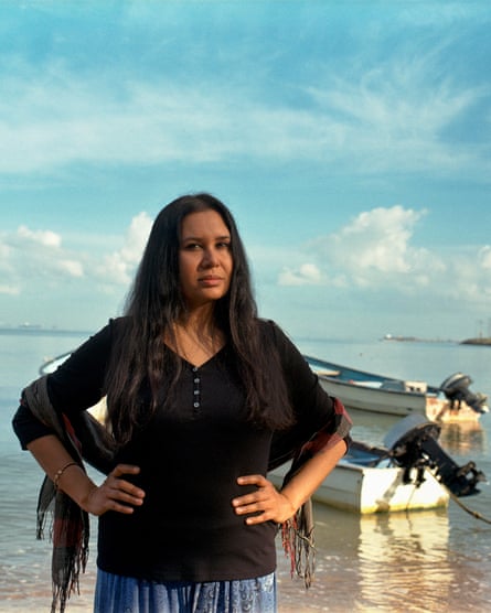 Dr Shobha Maharaj standing in front of the shore with two small motorboats in the water behind her