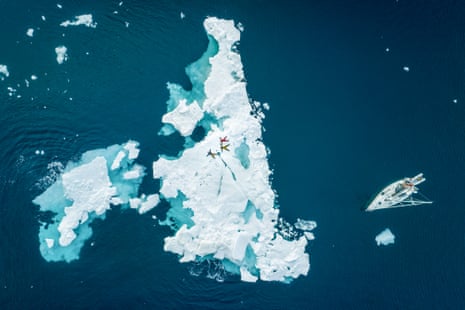 Overhead shot of three people lying on an ice sheet next to a small sailboat