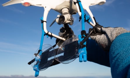 A drone with two large petri dishes attached against blue sky