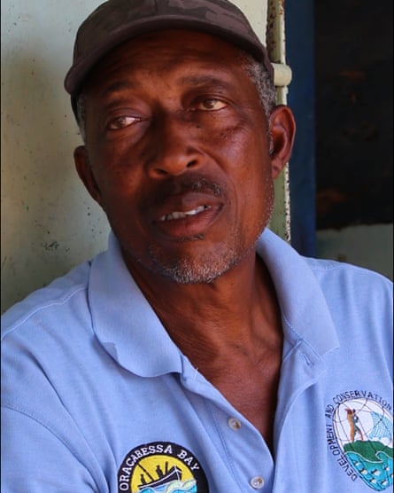 A man wearing a blue t-shiort bearing the logo of the Oracabessa Bay Fish Sanctuary and a badge that reads ‘development and conservation’.