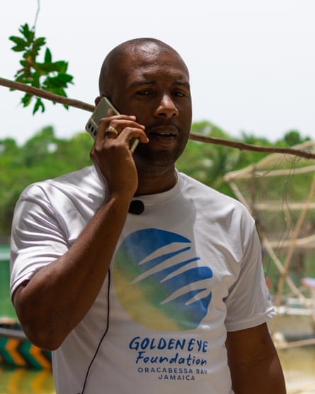 A man wearing a T-shirt with the logo of the GoldenEye Foundation speaks on a mobile phone