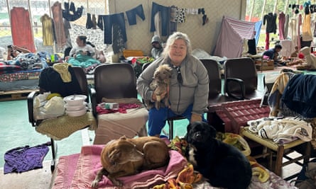 A woman sits with three dogs in a large room strewn with belongings