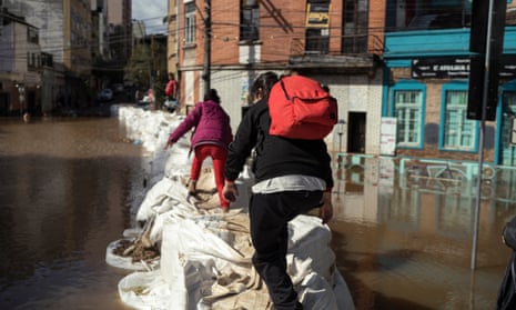 Two people clamber over a row of large full sacks in the middle of a flooded street