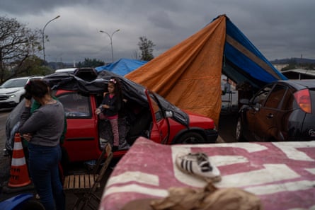 A woman and a child next to a car with a tarpaulin over it, alongside other cars and makeshift tents