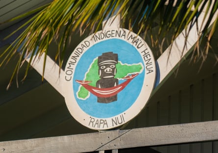 A painted sign in the eaves of a thatched building, featuring a statue and crescent-shaped ornament superimposed on an outline of the island