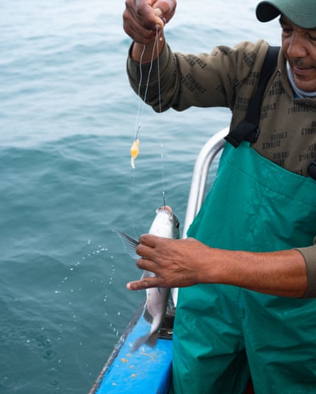 A man lifting a fish on a hook on to his boat. 