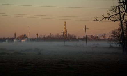 The lights, chimneys and gas tanks of a factory seen from a distance at dawn with mist on the ground