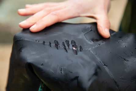 Someone showing abrasions and a hole on the shoulder of a black neoprene wetsuit