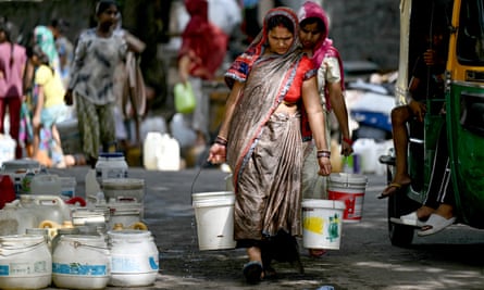 A woman carries vessels filled with water with more placed on the ground to the left