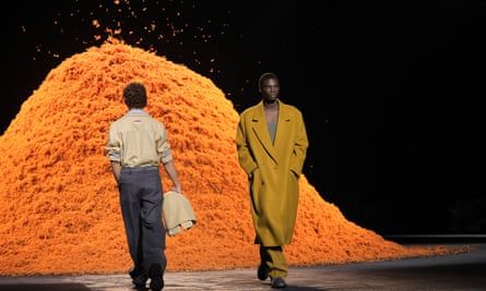 Models walking alongside a giant pile of orange cashmere at a fashion show in Milan