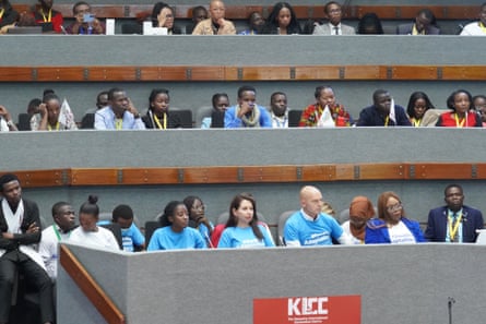 Verkooijen sitting in a blue T-shirt with the slogan “double adaptation” along with dozens of others, largely young Africans, listening to a speaker off camera  