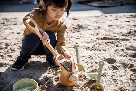 A child uses a sugarcane spade to put sand in a bucket on the beach