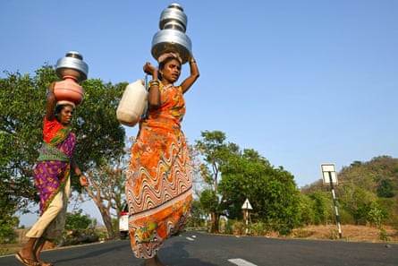 Women in colourful saris carry water pots across a road