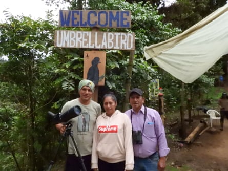 A young man and his parents stand below a hand-painted wooden sign reading “Welcome umbrellabird”