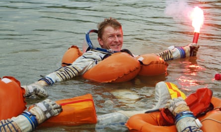 Tim Peake in water, held afloat by an orange lifejacket and holding a flare in his left hand