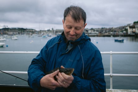 A man holds a fish he has just caught, on Falmouth pier